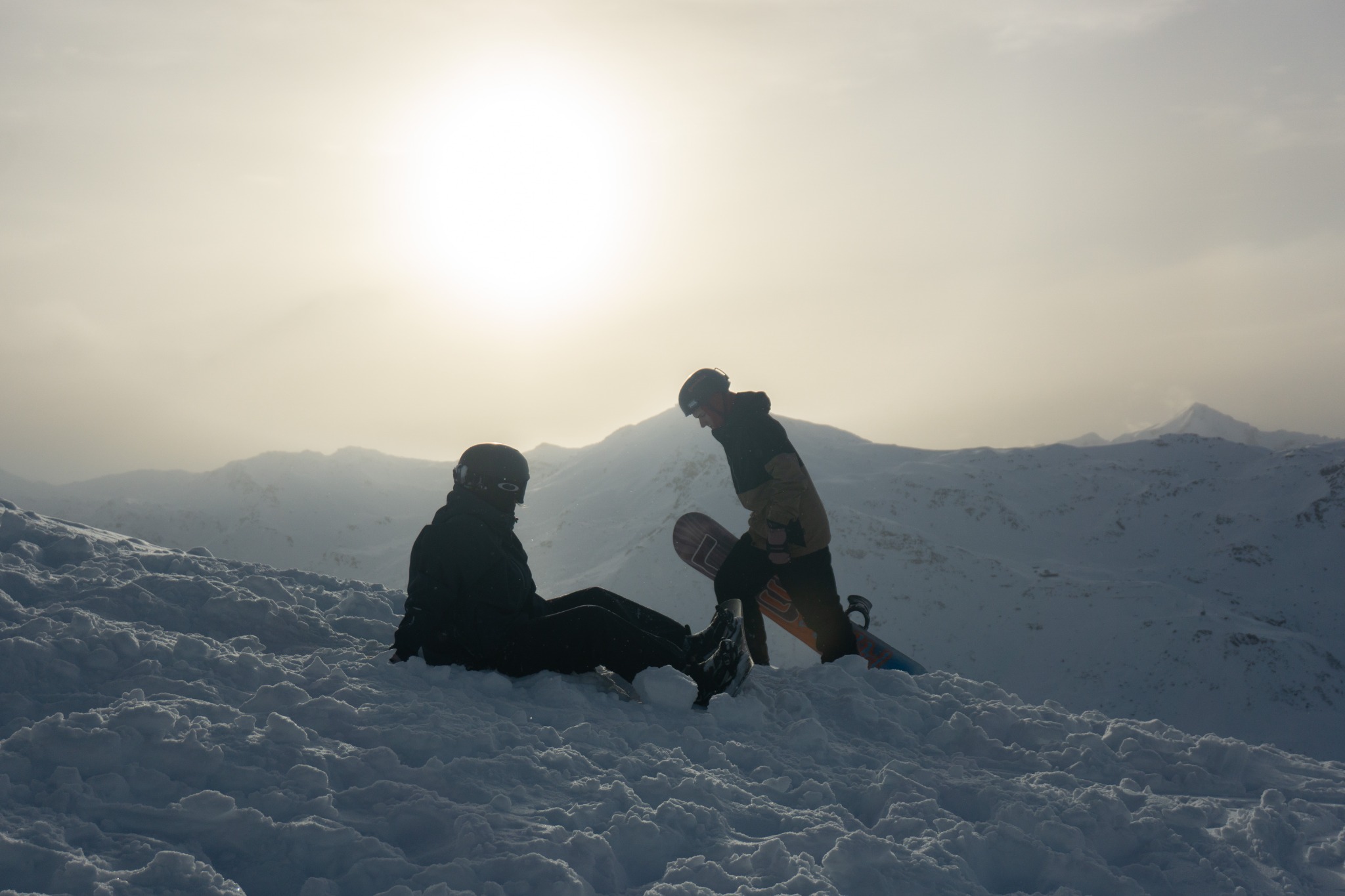 Two snowboarders pausing on a snowy ridge in soft golden light