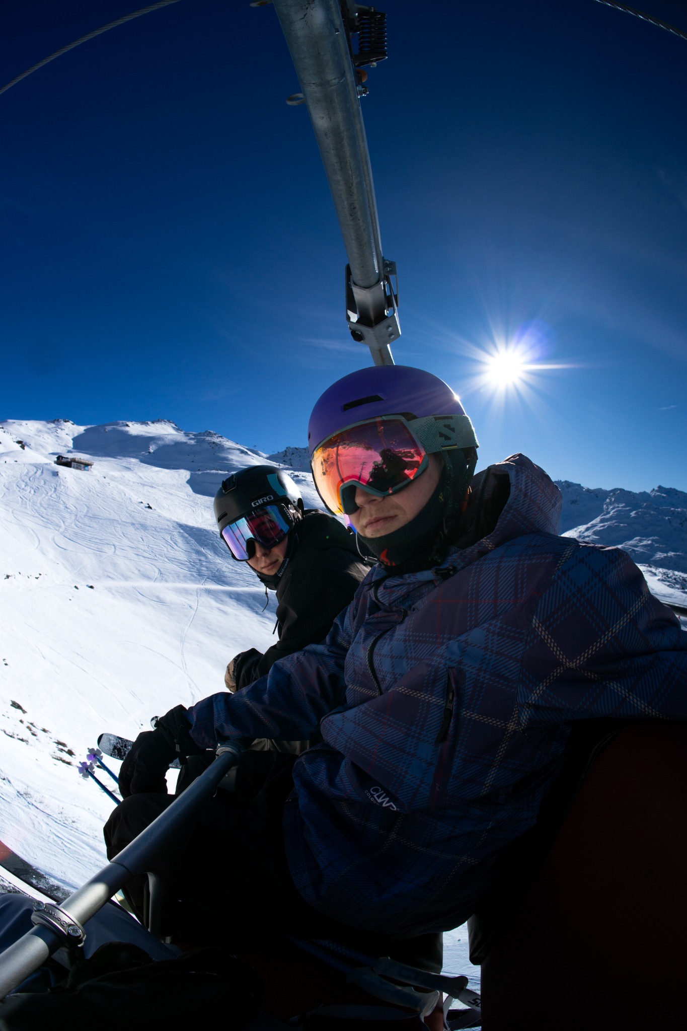 Two skiers together on a chairlift beneath a blue sky and bright alpine sunshine